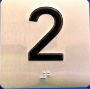 A stainless steel elevator jamb braille plate with the number 2 and the Avenir font.